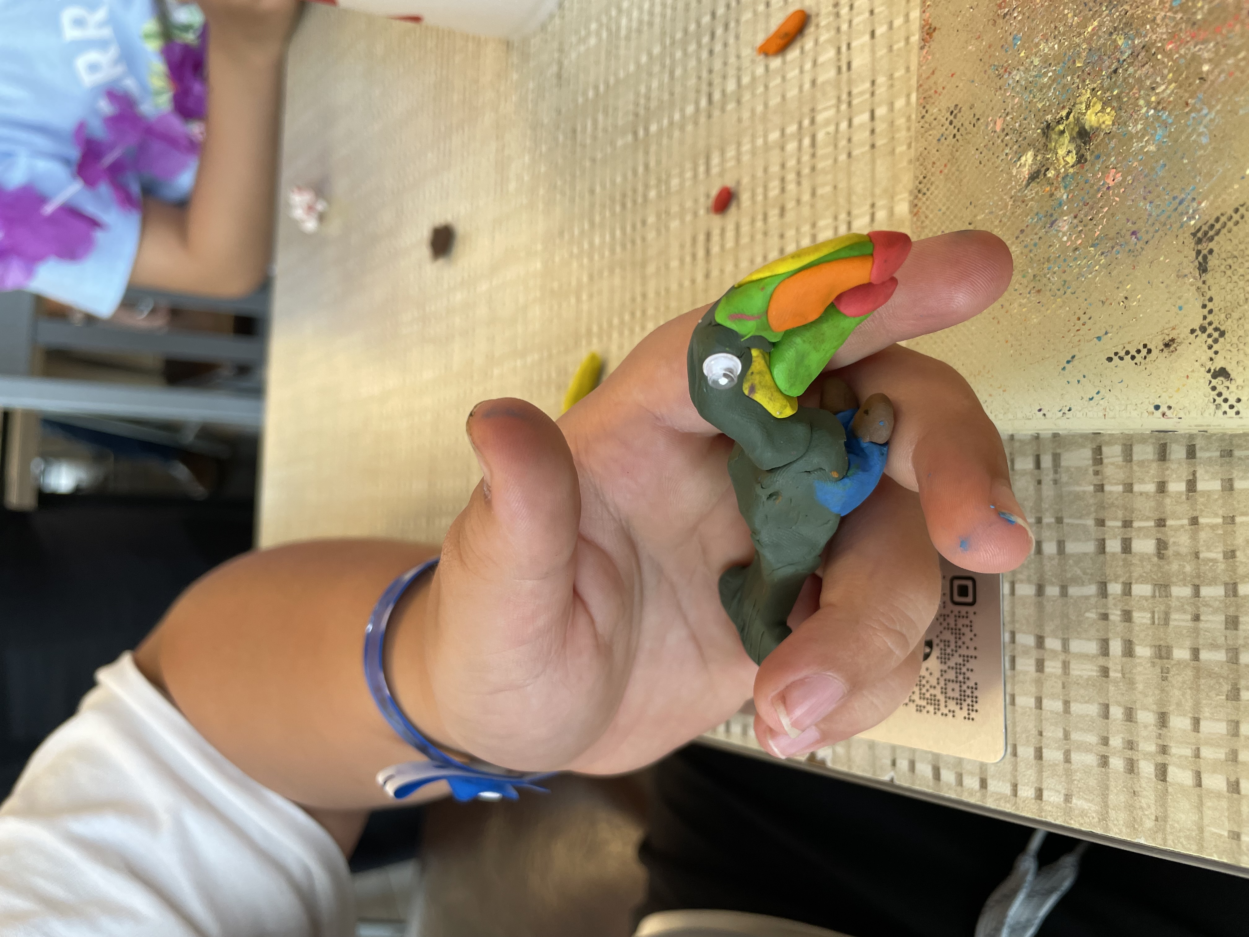 Child's hand holding a small colorful clay Toco Toucan with orange beak pieces nearby