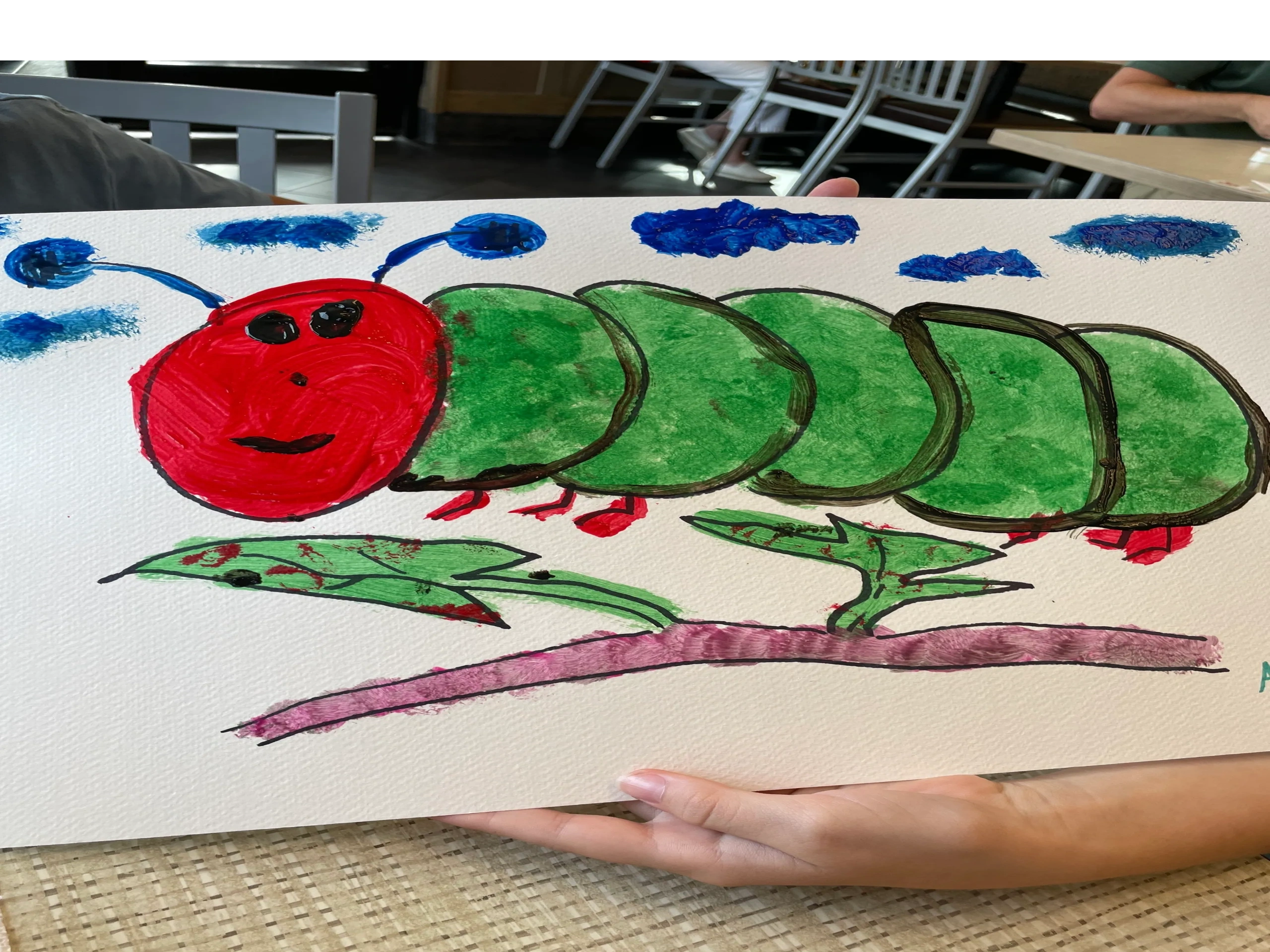 Child's colorful drawing of a caterpillar with red head, green body segments, and blue clouds